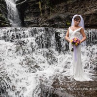 Creative Bridal Session color photograph with bride in an elegant full length pose on a rock outcrop next to a waterfall