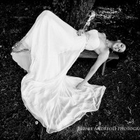 Creative Bridal Session black and white photograph with bride laying back on a bench and her bridal gown flowing to the ground