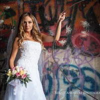 Creative Bridal Session with the Bride posing with flowers in front of a graffiti painted wall. 3/4 length portrait lit by window light